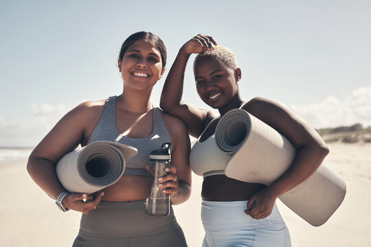 Friends who sweat together, stick together. Shot of two young women holding their yoga mats while on the beach.