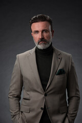 Fototapeta premium Portrait of a stylish elegant senior businessman with a beard and casual business clothes in photo studio isolated on dark background gesturing with hands