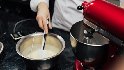 Closeup of chef stirring mixing cream in bowl while standing in the kitchen. Cake making, pastry...