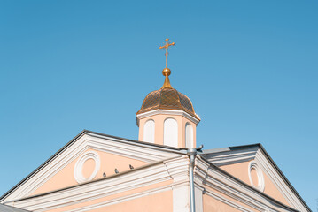 Church with golden dome and cross against clear blue sky. Exterior of an ancient religious building outdoors. Faith and religion concept