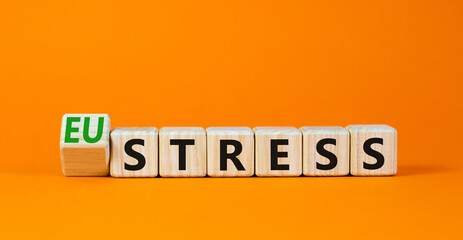 Eustress or stress symbol. Turned the wooden cube and changed the concept word Eustress to Stress. Beautiful orange table orange background, copy space. Psychlogical and stress or eustress concept.