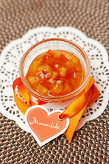 A bowl with marmalade made of organic oranges with a ribbon and a tag in the form of a heart on a wicker tablecloth. Natural, home product.