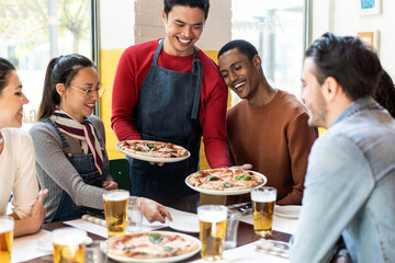 Confidant waiter serving delicious pizzas margherita to multicultural friends in cozy pizzeria...