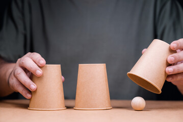 Closeup man playing a shell game, three cups with wooden ball, and reveal where the right position...