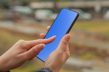 Woman hand holding smartphone outside and touching blue screen.