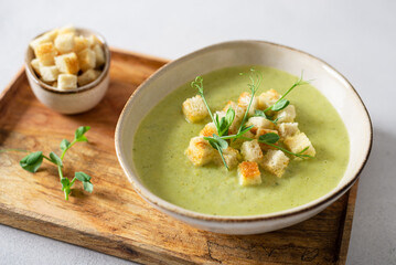 Detox cream soup of green vegetables broccoli, green peas, spinach served with crutons and micro greens on grey concrete background. Spring detox recipe, healthy food concept. Close up