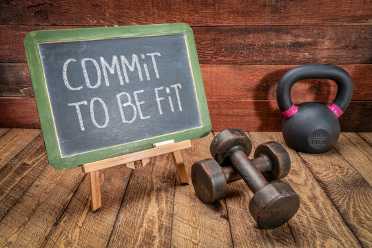 commit to be fit -  inspirational concept, white chalk text on a slate blackboard sign against weathered rustic wood with a dumbbells and kettlebell