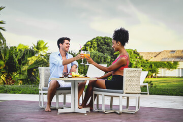 Joyful couple of vacation having breakfast sitting on a table in the terrace - newlyweds toast...
