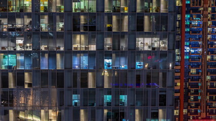 Night aerial view of office or apartment building glass window facade with illuminated lighted workspace rooms timelapse.