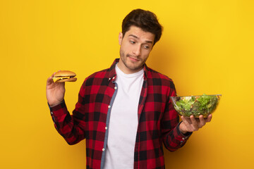 Portrait of Funny Guy Holding Burger And Vegetable Salad