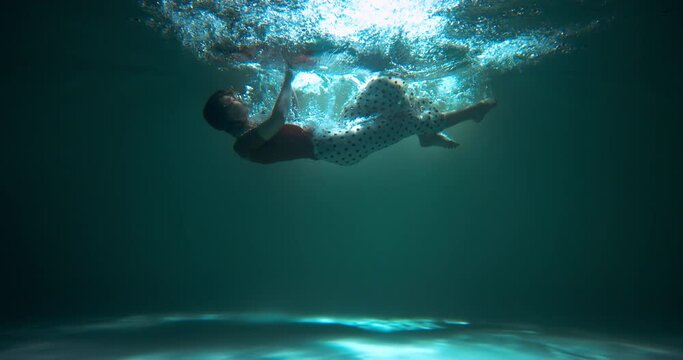 AGE OF DEPRESSION Amazing underwater shot, beautiful young woman falls sinking helpless under blue water slow motion.