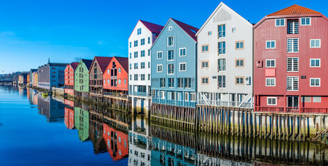 Wide panoramic view of old colorful wooden houses with reflections in river Nidelva in the Brygge district in Trondheim, Norway