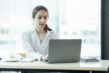 Cropped image of professional Asian businesswoman working at her office via laptop, young female manager using portable computer device while sitting at modern loft, flare light, work process concept