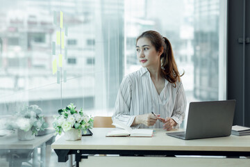 Cropped image of professional Asian businesswoman working at her office via laptop, young female manager using portable computer device while sitting at modern loft, flare light, work process concept