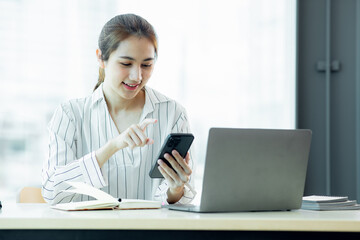 Excited Asian young woman using phone and laptop sitting on a desk office in the day at office