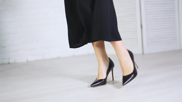 Elegant classic black shoes demonstration. Woman in long black skirt showing the high-heeled stiletto footwear. White backdrop.