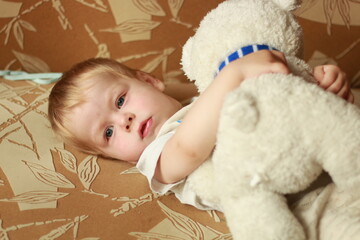a little boy lies with a bear in an embrace on the sofa. sad kid