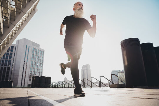 Photo of confident purposeful retired man black sportswear enjoying sunrise running fast outside urban city street