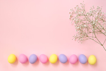 Top view layout of colorful painted Easter eggs and spring baby's breath flowers on pink background. Greeting card, poster, banner for Happy Easter. Copy space for your text.
