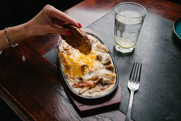 hot skillet with chicken and mushrooms in a creamy sauce. Woman's hand dipping bread into a dish