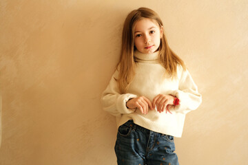 little beautiful girl 9 years old schoolgirl portrait on a beige background in a white sweater pensive model long hair