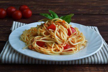Spaghetti pasta with tomatoes and basil on a wooden table.