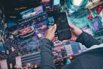 Girl on balcony of high floor apartment holding smartphone with Financial stock market graph on the screen. City at night in the background. Stock Exchange