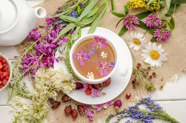 Herbal tea with rosehip, chamomile and meadowsweet in a white cup on a white wooden table with flowers