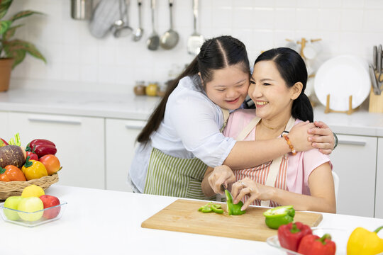 down syndrome teenage girl hugging her mother while cooking food in the kitchen