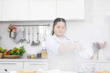 down syndrome teenage girl throwing and sprinkling white flour for making a bread or cooking food...