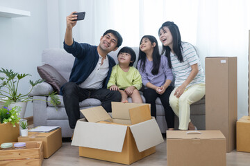 Happy family couple hugging adorable kids, sitting on couch at home together, taking selfie on phone. Medium shot. Family photo, celebrate moving day to new home, heap of boxes lies on floor.