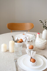 Easter table setting. Easter egg with bunny ears made of napkin on plate, cutlery, decor on desk with linen tablecloth.