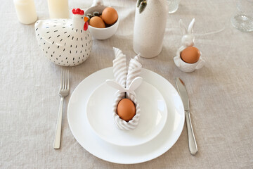 Easter egg with bunny ears made of napkin on plate and cutlery on linen tablecloth.