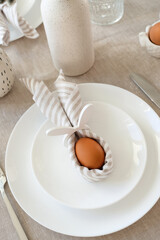 Fototapeta na wymiar Elegant Easter table setting. Easter egg in bunny napkin on plate with cutlery