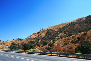 Early afternoon sun over the golden grass hill with trees and shrubs and electrical power lines