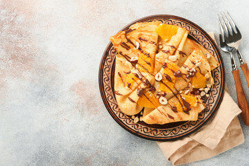 Crepes suzette with oranges and chocolate. Thin crepes with chocolate spread, hazelnuts and orange slices fruit in plate for breakfast on old concrete rustic table background. Copy space. Top view