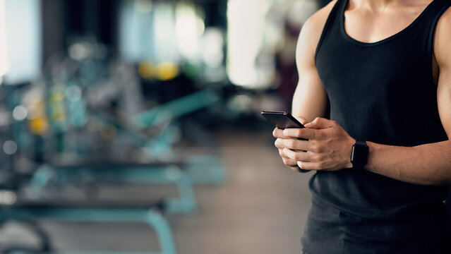 Cropped Shot Of Muscular Man Wearing Smartwatch Using Smartphone At Gym - Powered by Adobe
