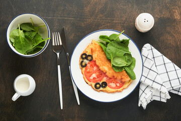 Omelette with tomatoes, black olives, cottage cheese and green spinach herbs on white plate on old wooden rustic dark background. Delicious breakfast. Healthy breakfast food. Top view.