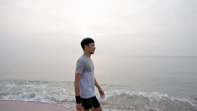 4K 50fps, Young Asian man walking by the sea in the morning with good weather, clear skies, in the background with the morning sun rising, popular tourist attraction