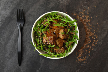 Close up of pieces of beef stewed in soy sauce with arugula in asian style on black background.