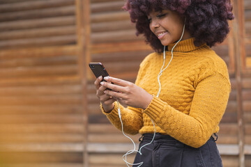 Young afro woman listening to music on her mobile device. Concept of young man enjoying music outdoors.