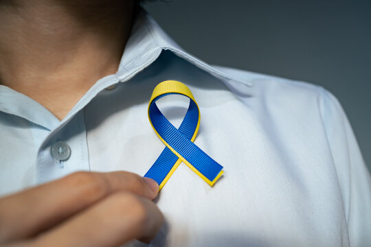 A man attach blue and yellow ribbon for Ukraine to a shirt.