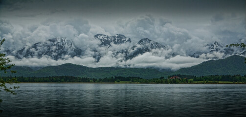 See mit Bergen im Hintergrund, die in üppige Wolken gehüllt sind. Horizontales Banner mit geheimnisvoller Landschaft