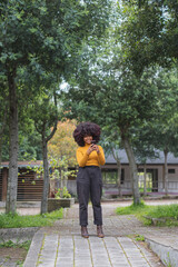 Young Afro woman texting on her cell phone. Concept of young afro American girl outdoors checking chats on her device.