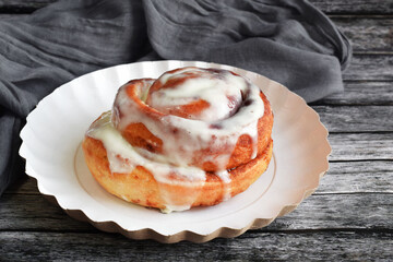 Cinnamon bun with cream on a white plate. Grey wooden background.