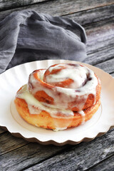 Cinnamon bun with cream on a white plate. Grey wooden background.