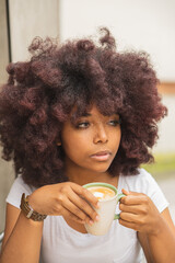 Close-up of a young afro woman in a coffee shop enjoying a delicious coffee. With the concept of relaxing time of a person in an openwork place.