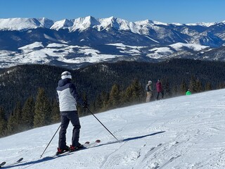 Skier on the slope enjoying top view of winter landscape. Rocky mountains covered with snow in...