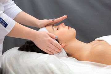 The doctor holds his palms over the girl's face while performing a facial massage.Cosmetologist in the process of working with a client.A young woman enjoys a facial massage while lying on a couch.