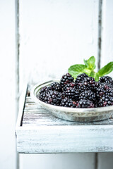 Blackberries in a silver plate on a white rustic background.